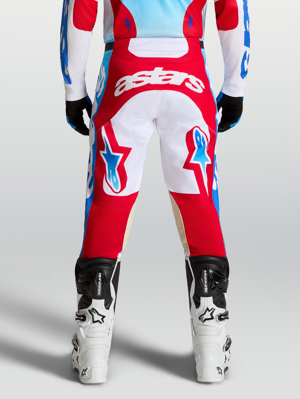 Alpinestars Spodnie Racer Hunt, spodnie motocrossowe czerwone i białe, widok z tyłu na motocyklistę, niebieskie akcenty, wstępnie zakrzywiony krój.