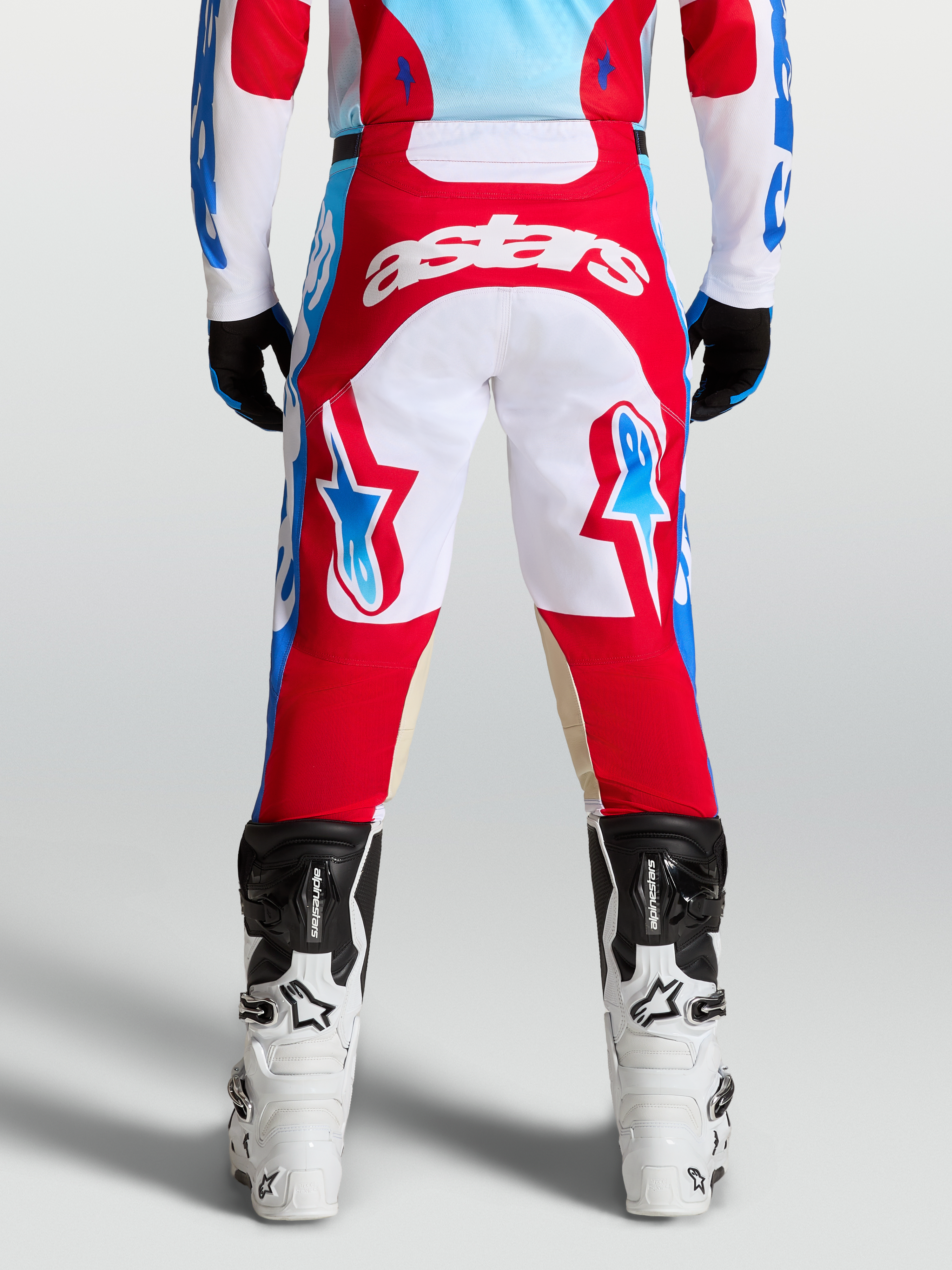 Alpinestars Spodnie Racer Hunt, spodnie motocrossowe czerwone i białe, widok z tyłu na motocyklistę, niebieskie akcenty, wstępnie zakrzywiony krój.