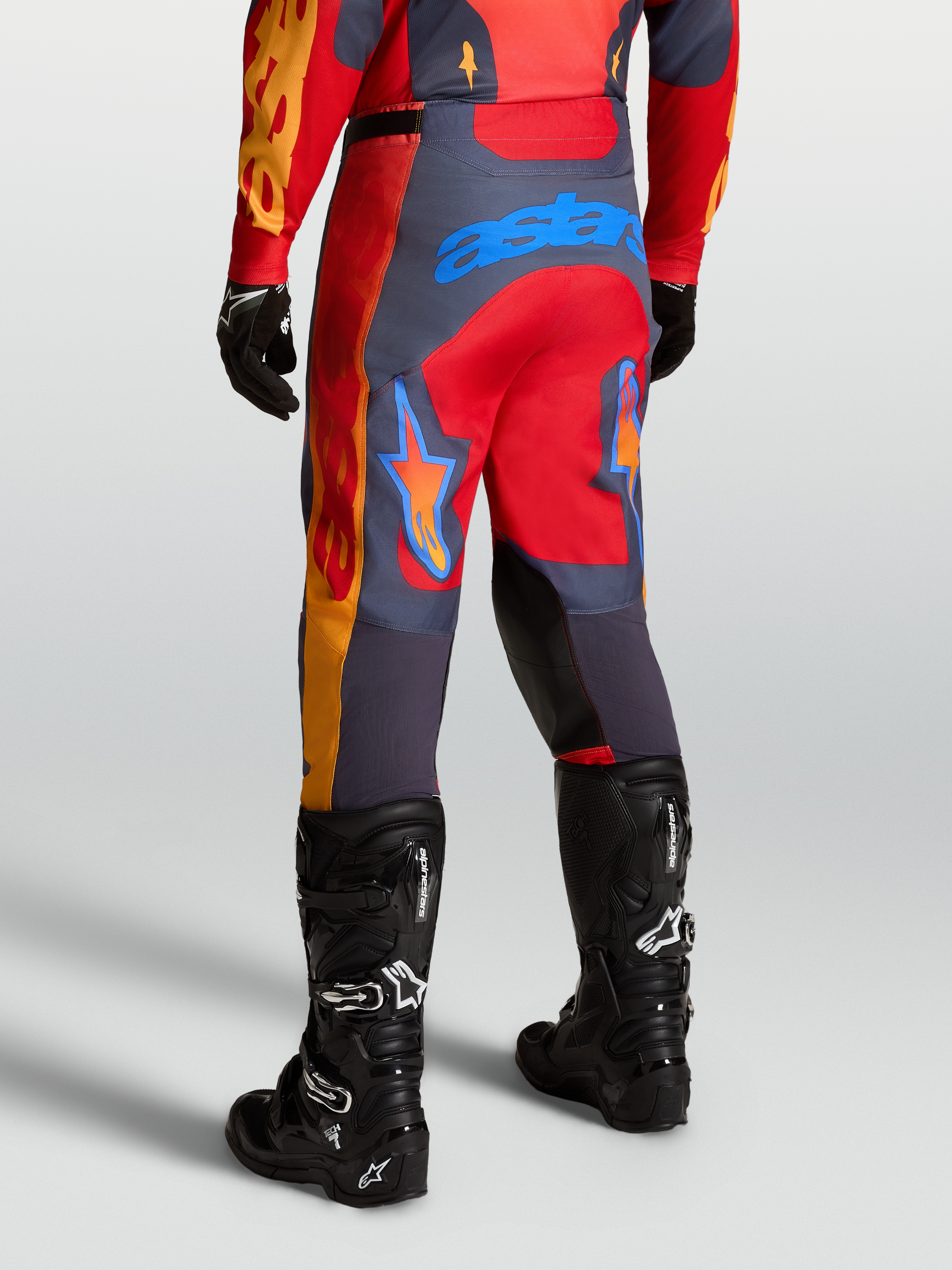 Alpinestars Spodnie Racer Hunt, męskie spodnie motocrossowe, czerwone i szare, widok od tyłu w pozycji sportowej.