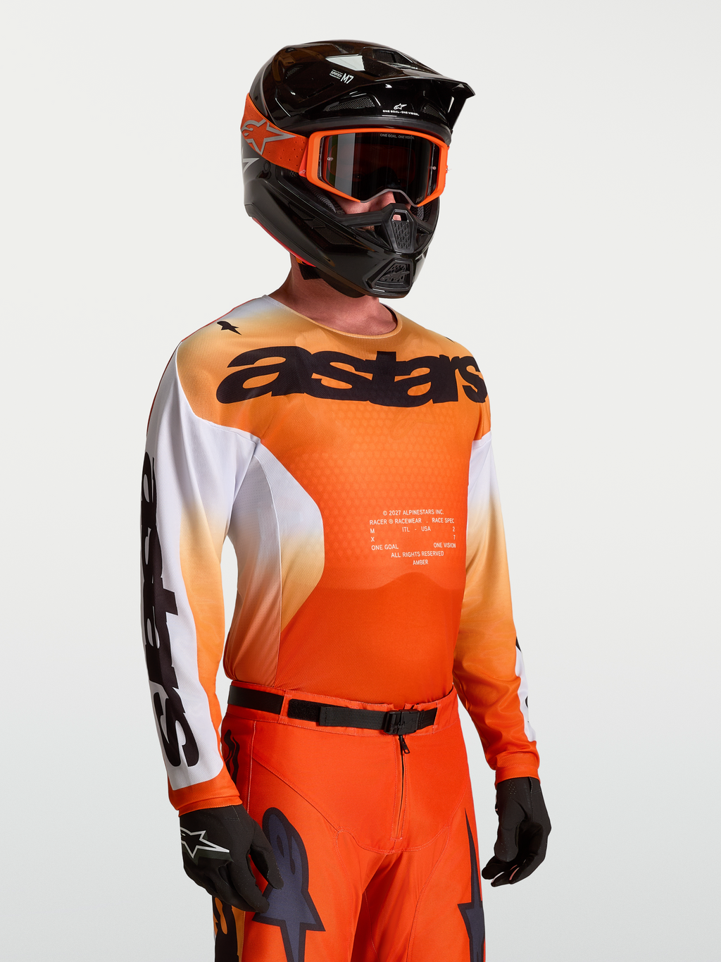 Alpinestars koszulka Racer Amber, męska koszulka motocrossowa, pomarańczowa i biała, lekka, model w kasku i goglach.
