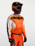 Alpinestars koszulka Racer Amber, męska koszulka motocrossowa, pomarańczowa i biała, lekka, model w kasku i goglach.