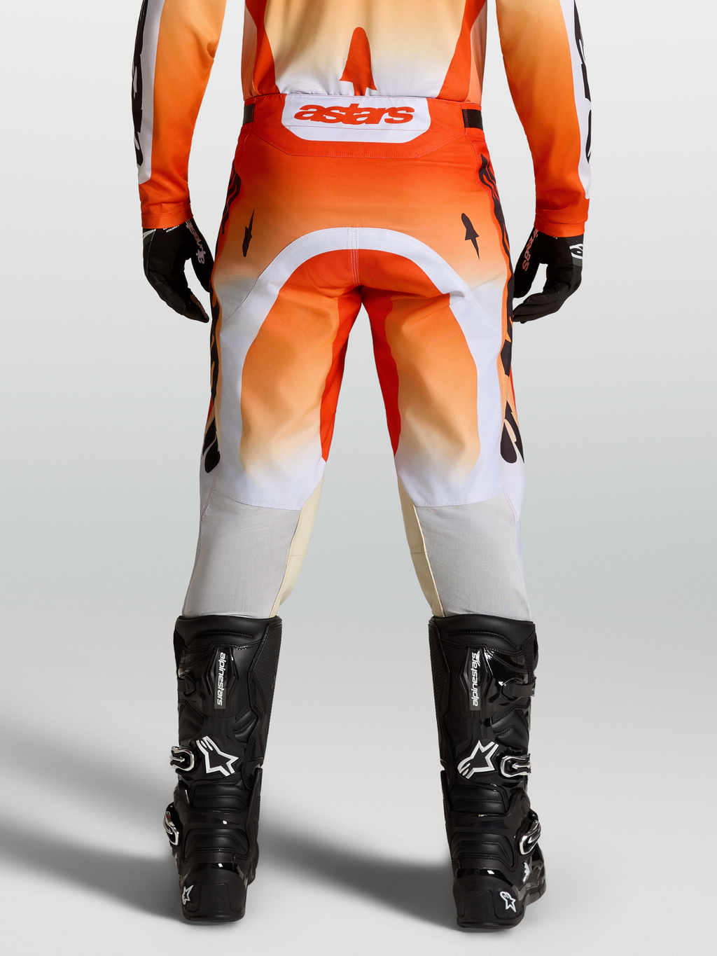 Alpinestars Spodnie Racer Amber, męskie spodnie motocrossowe, czerwone i białe, widok od tyłu na modelu z czarnymi butami.