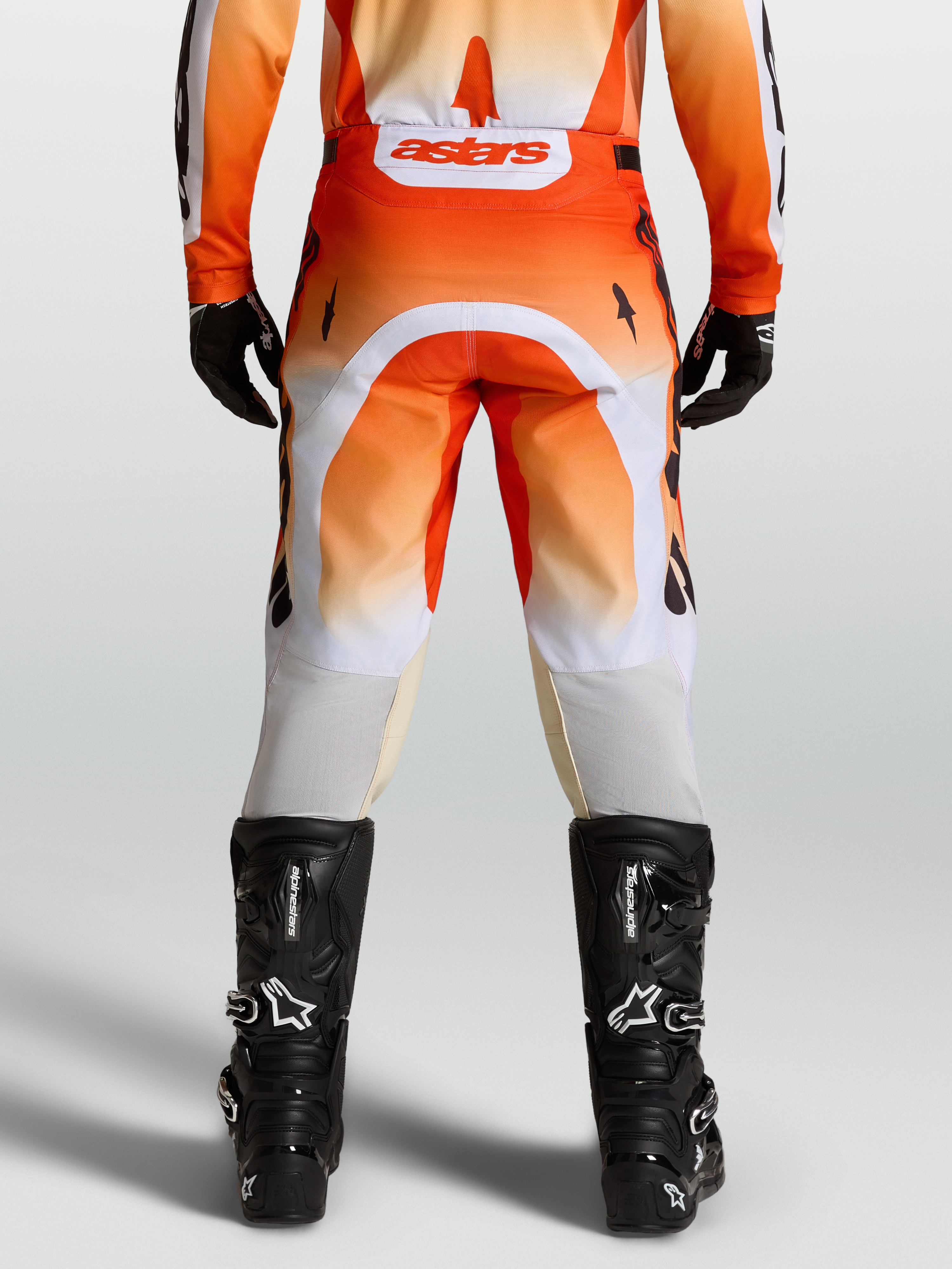 Alpinestars Spodnie Racer Amber, męskie spodnie motocrossowe, czerwone i białe, widok od tyłu na modelu z czarnymi butami.