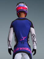 Koszulka Alpinestars Techstar Knif 2026, widok z tyłu zawodnika motocrossowego, kolorystyka Black Light Gray Purple, fioletowy panel na plecach z różowym logo, jasnoszare rękawy z czarnymi akcentami i laserowymi perforacjami, różowo-fioletowy kask i czarne rękawice