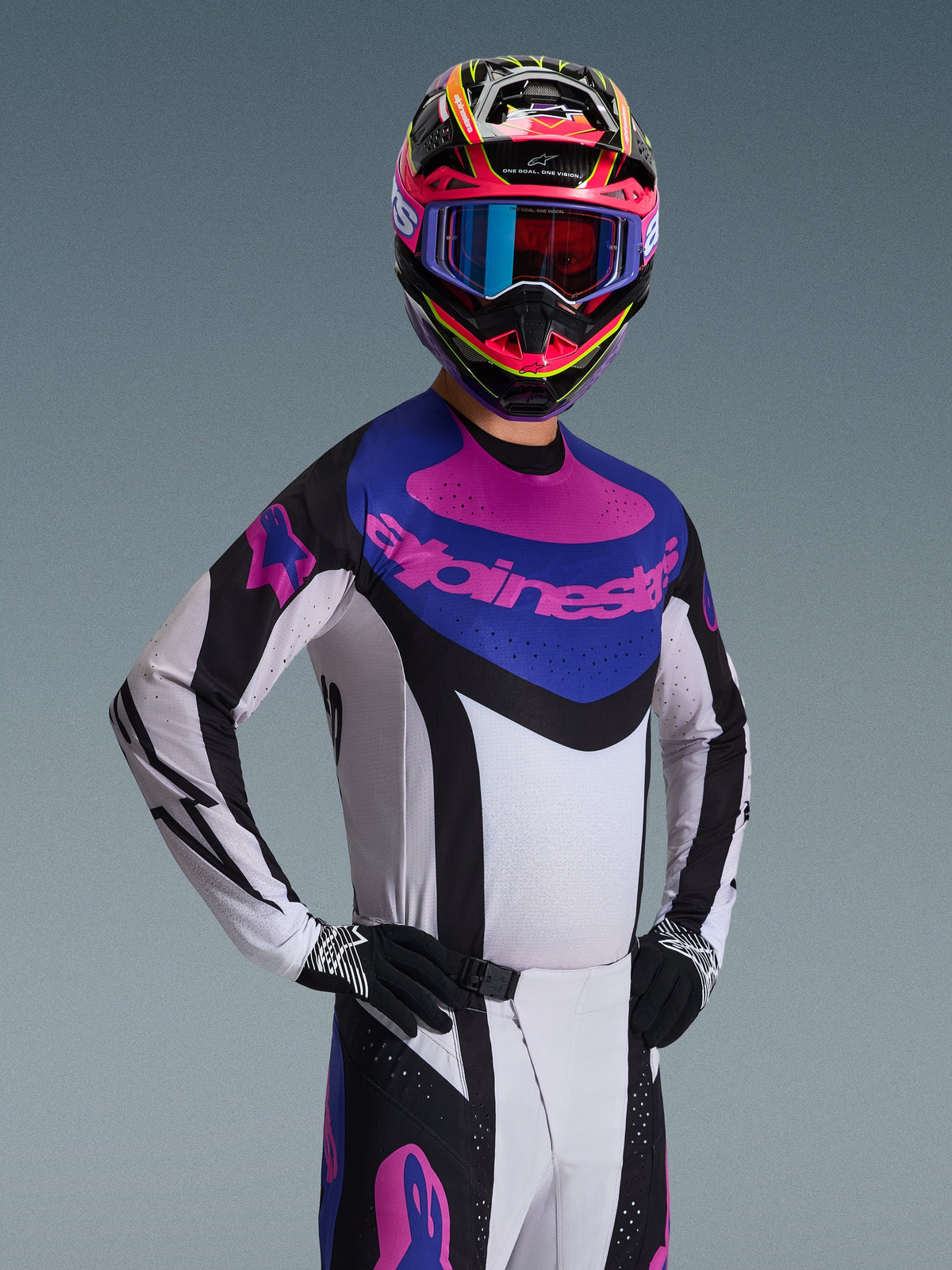 Alpinestars Techstar Knif Jersey 2026, koszulka motocrossowa, czarna, jasnoszara i fioletowa, noszona przez zawodnika w pełnym stroju, biały korpus z czarnymi akcentami, niebieski panel na klatce piersiowej z fioletowym logo Alpinestars, wyczynowy krój wyścigowy do jazdy terenowej