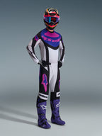 Zawodnik motocrossowy w koszulce Alpinestars 2026 Techstar Knif w kolorze Black Light Gray Purple, pasujące spodnie z dużymi różowymi logotypami, fioletowe buty i wielokolorowy kask z niebieskimi goglami, pełny zestaw wyścigowy do jazdy terenowej
