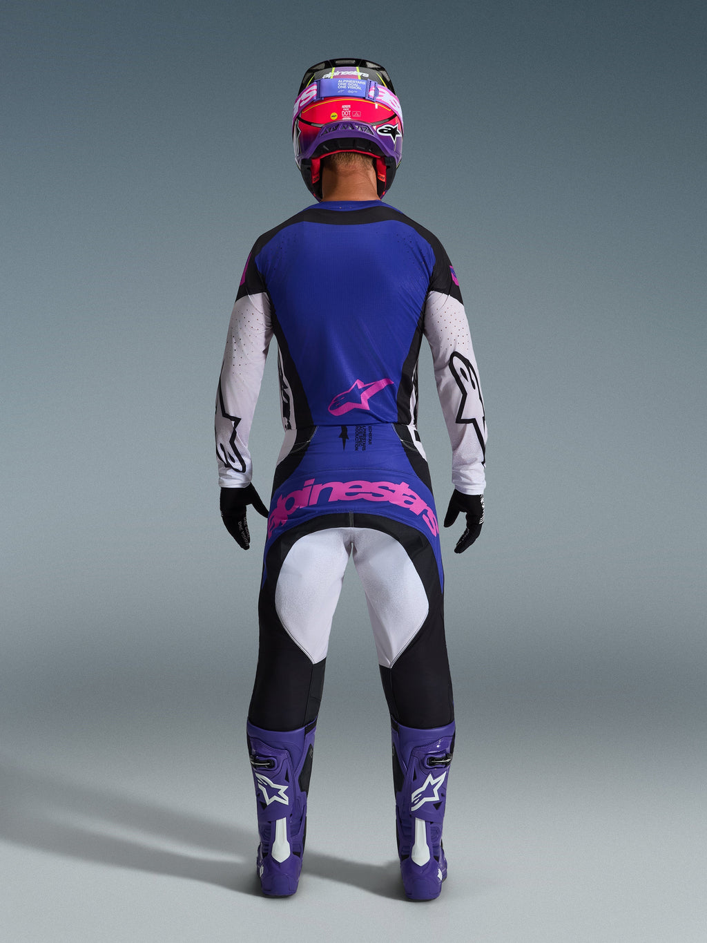 Zawodnik motocrossowy widziany od tyłu w koszulce 2026 Techstar Knif, kolor Black Light Gray Purple, pasujące spodnie motocrossowe z różowym logotypem, fioletowe buty i kask, profesjonalny, wysokowydajny zestaw odzieży off-road