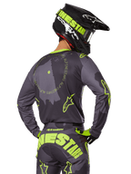 Motocyklista motocrossowy widziany od tyłu w zestawie Racer Hollow 2025, szara koszulka z neonowożółtym napisem w kształcie koła i logo z gwiazdą, pasujące szaro-żółte spodnie z wyraźnym brandingiem na siedzeniu, czarno-limonkowy kask, dopasowany strój do wyścigów terenowych