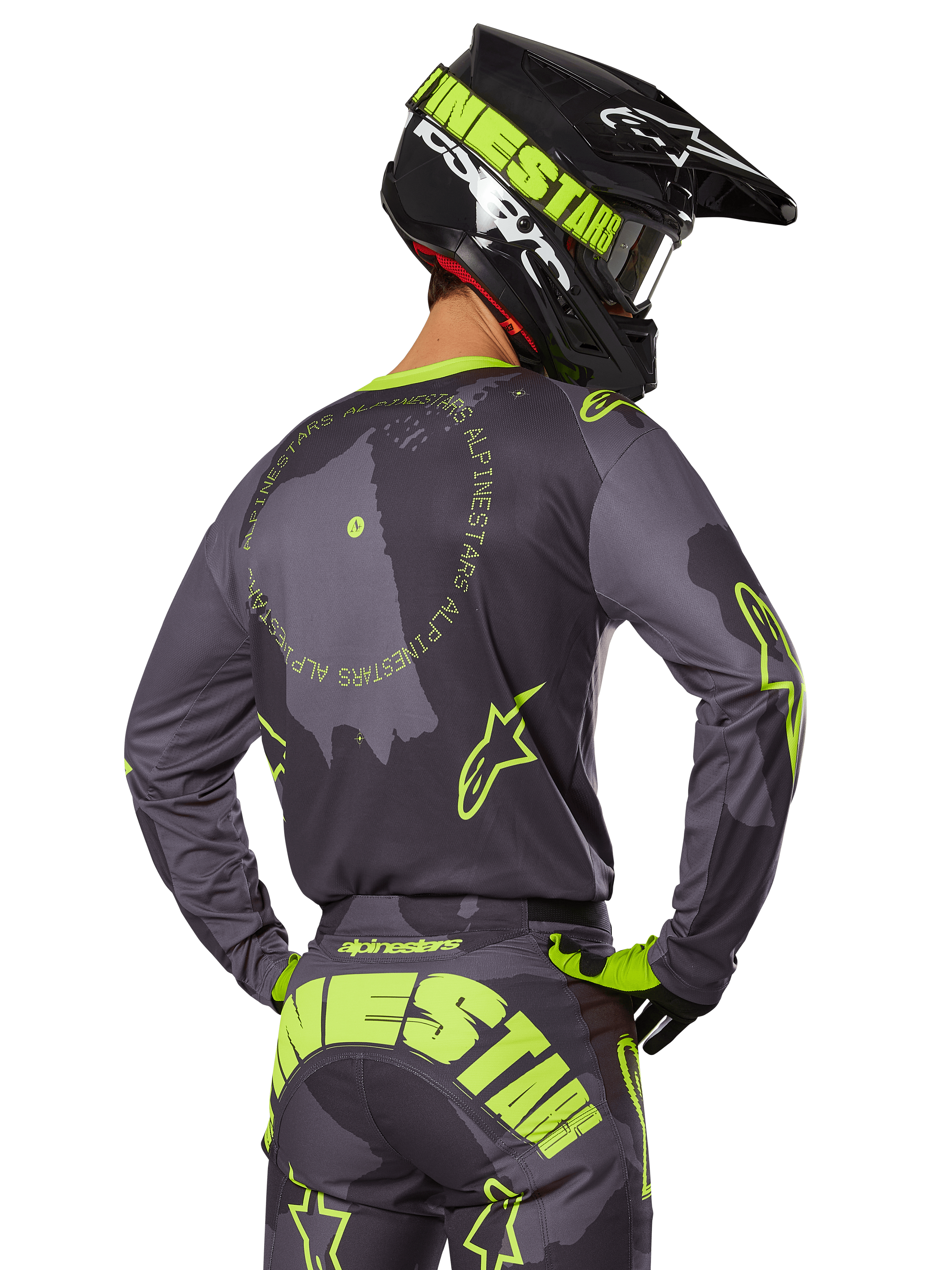 Motocyklista motocrossowy widziany od tyłu w zestawie Racer Hollow 2025, szara koszulka z neonowożółtym napisem w kształcie koła i logo z gwiazdą, pasujące szaro-żółte spodnie z wyraźnym brandingiem na siedzeniu, czarno-limonkowy kask, dopasowany strój do wyścigów terenowych