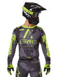 Alpinestars 2025 Racer Hollow Jersey, koszulka motocrossowa, ciemne moro i neonowy żółty, noszona z dopasowanymi spodniami, czarno-żółtym kaskiem z goglami i czarnymi rękawicami, logo Alpinestars i wzór kamuflażu