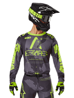 Alpinestars 2025 Racer Hollow Jersey, koszulka motocrossowa, ciemne moro i neonowy żółty, noszona z dopasowanymi spodniami, czarno-żółtym kaskiem z goglami i czarnymi rękawicami, logo Alpinestars i wzór kamuflażu