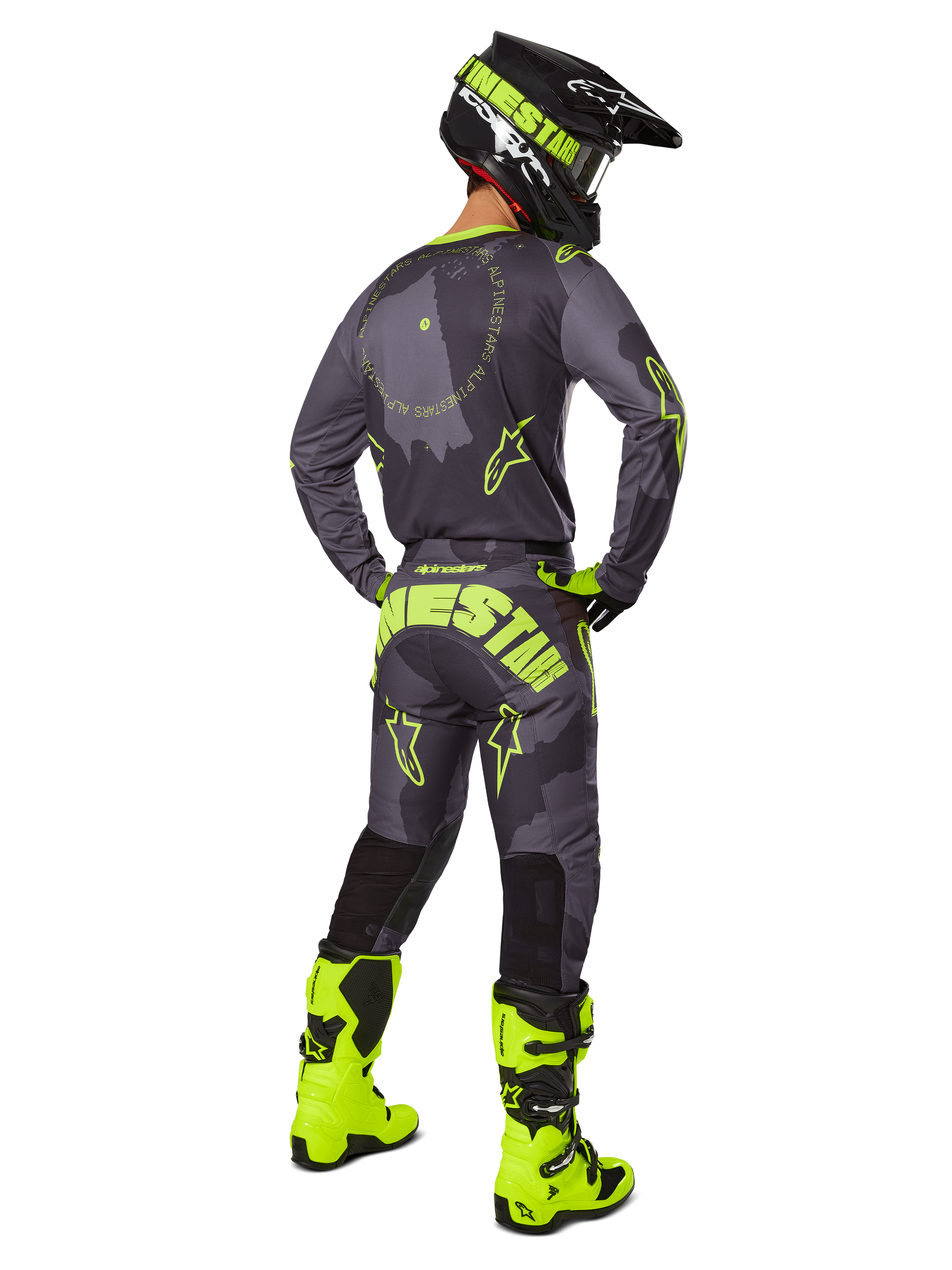 Widok z tyłu zawodnika motocrossowego w zestawie Racer Hollow 2025 w kolorze Dark Camo Yellow Fluo, szara koszulka moro z jaskrawożółtymi akcentami, pasujące spodnie z wyraźnym logo na siedzeniu, jaskrawożółte buty fluo i czarny kask z żółtymi goglami.