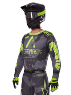 Zestaw Racer Hollow 2025 Alpinestars, koszulka i spodnie motocrossowe w kolorze szarym i neonowym żółtym, zestawiony z czarnym kaskiem, goglami i rękawicami, wyrazisty fluorescencyjny żółty branding Alpinestars i grafiki gwiazd na wzorzystym szarym tle, profesjonalny wygląd wyścigowy off-road