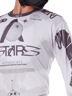 Zbliżenie na koszulkę Alpinestars 2025 Racer Hollow, biało-szara z czarnymi nadrukami graficznymi, logo globu i kodem binarnym, techniczna odzież motocrossowa do jazdy terenowej