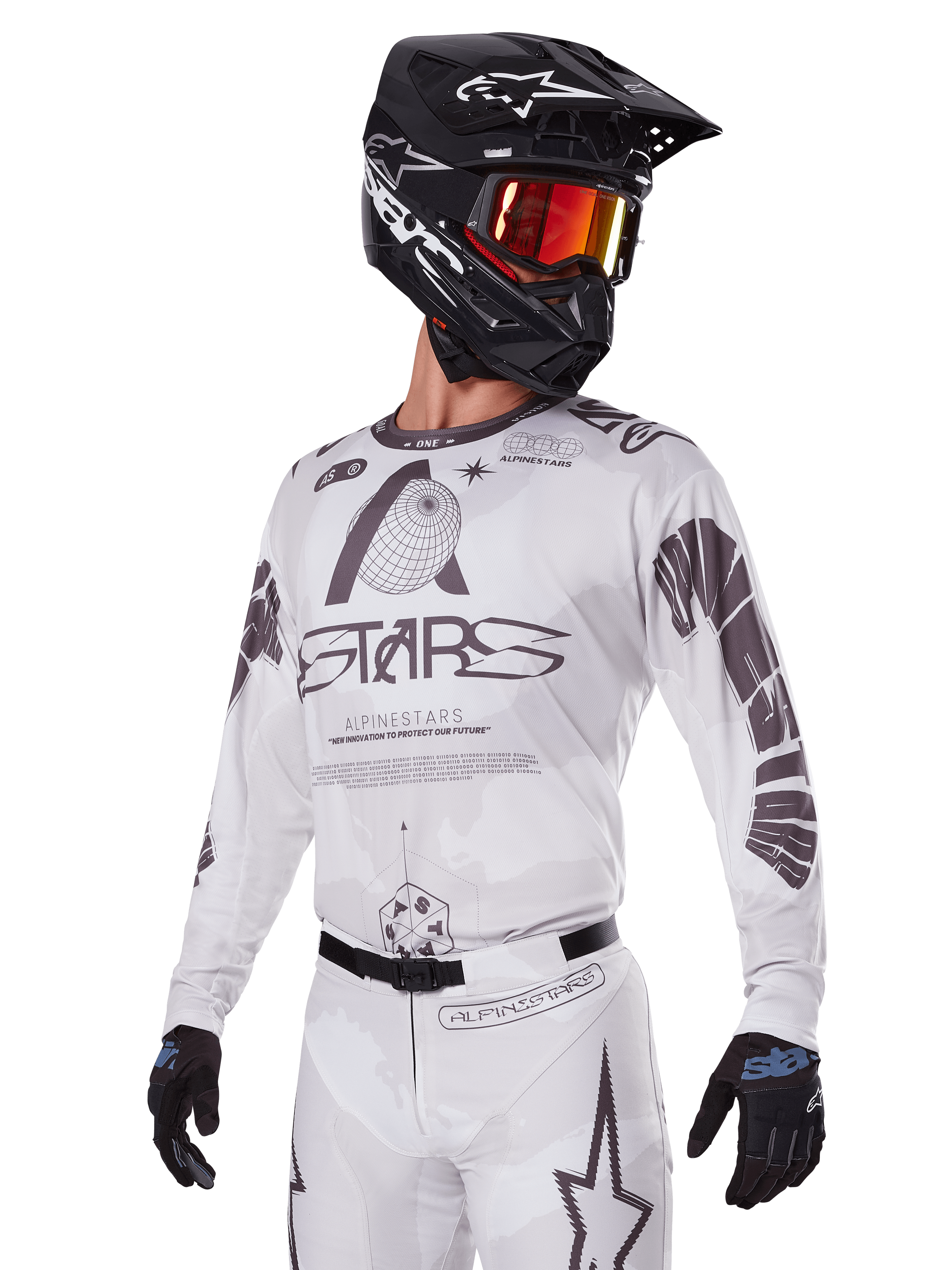 Zestaw Alpinestars 2025 Racer Hollow, koszulka i spodnie motocrossowe, białe z czarnymi i szarymi grafikami, z brandingiem „ASTARS” i motywami ażurowego globu, w połączeniu z czarnym kaskiem, czerwonymi lustrzanymi goglami i czarnymi rękawicami, zaprojektowany do wyczynowej jazdy off-road