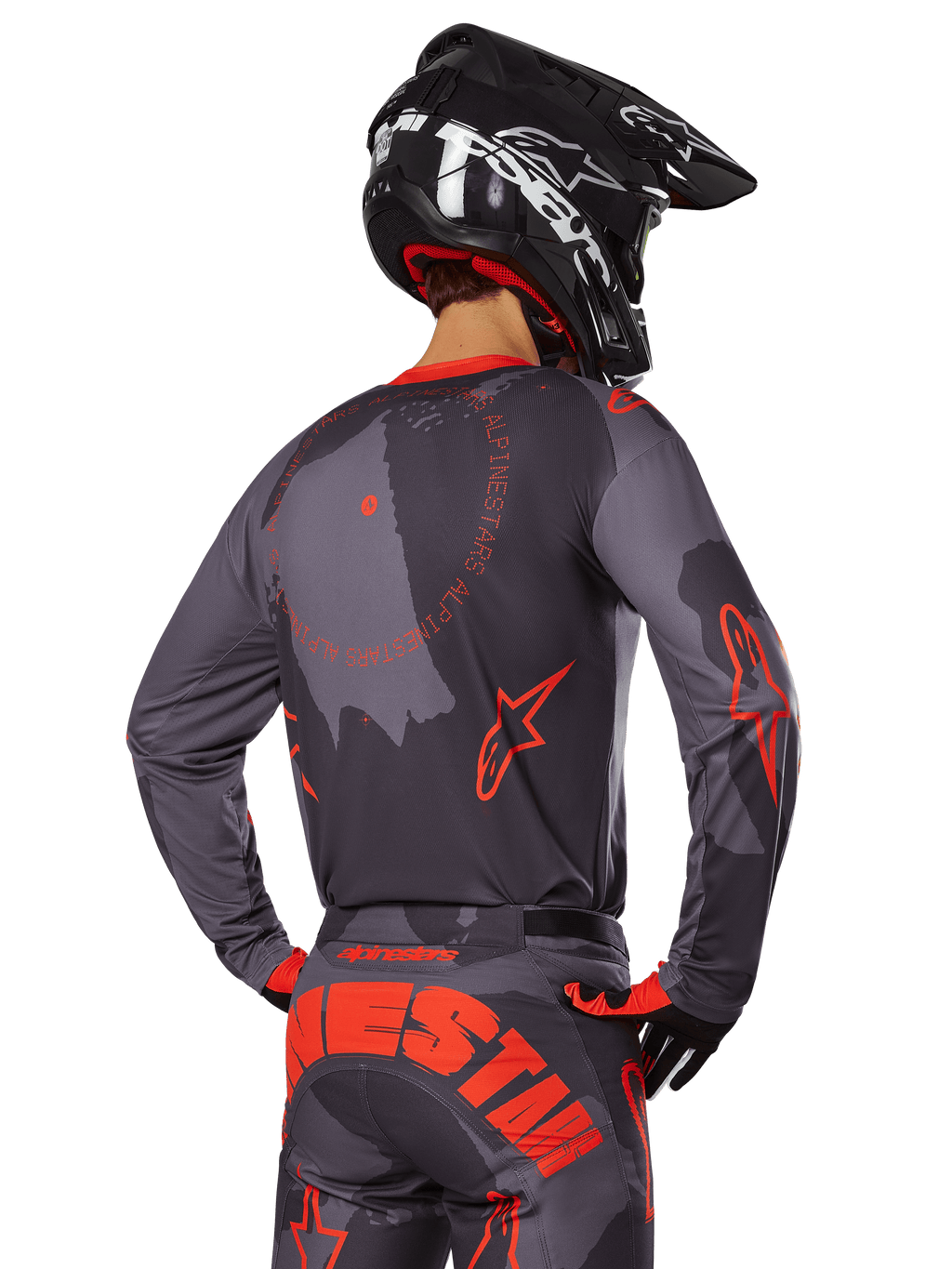 Alpinestars 2025 Racer Hollow Jersey, widok z tyłu motocyklisty w stroju Gray Camo i Orange Fluo, pasujące spodnie camo z dużym pomarańczowym napisem Alpinestars i czarny kask, profesjonalny design odzieży terenowej