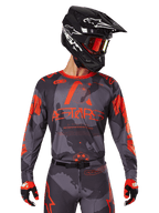 Alpinestars 2025 Racer Hollow Jersey, koszulka motocrossowa, szary kamuflaż i jaskrawy pomarańczowy, zestaw z pasującymi spodniami i rękawicami, czarny kask z białymi grafikami i goglami, wyraziste logo ASTARS, ochronna odzież do wyścigów terenowych