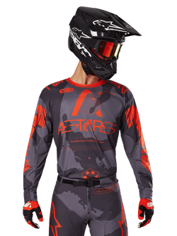 Alpinestars 2025 Racer Hollow Jersey, Motocross Jersey, Gray Camo and Orange Fluo, worn with matching gear set including pants and gloves, featuring a black helmet with white graphics and goggles, bold ASTARS branding, protective off-road racing sportswear
