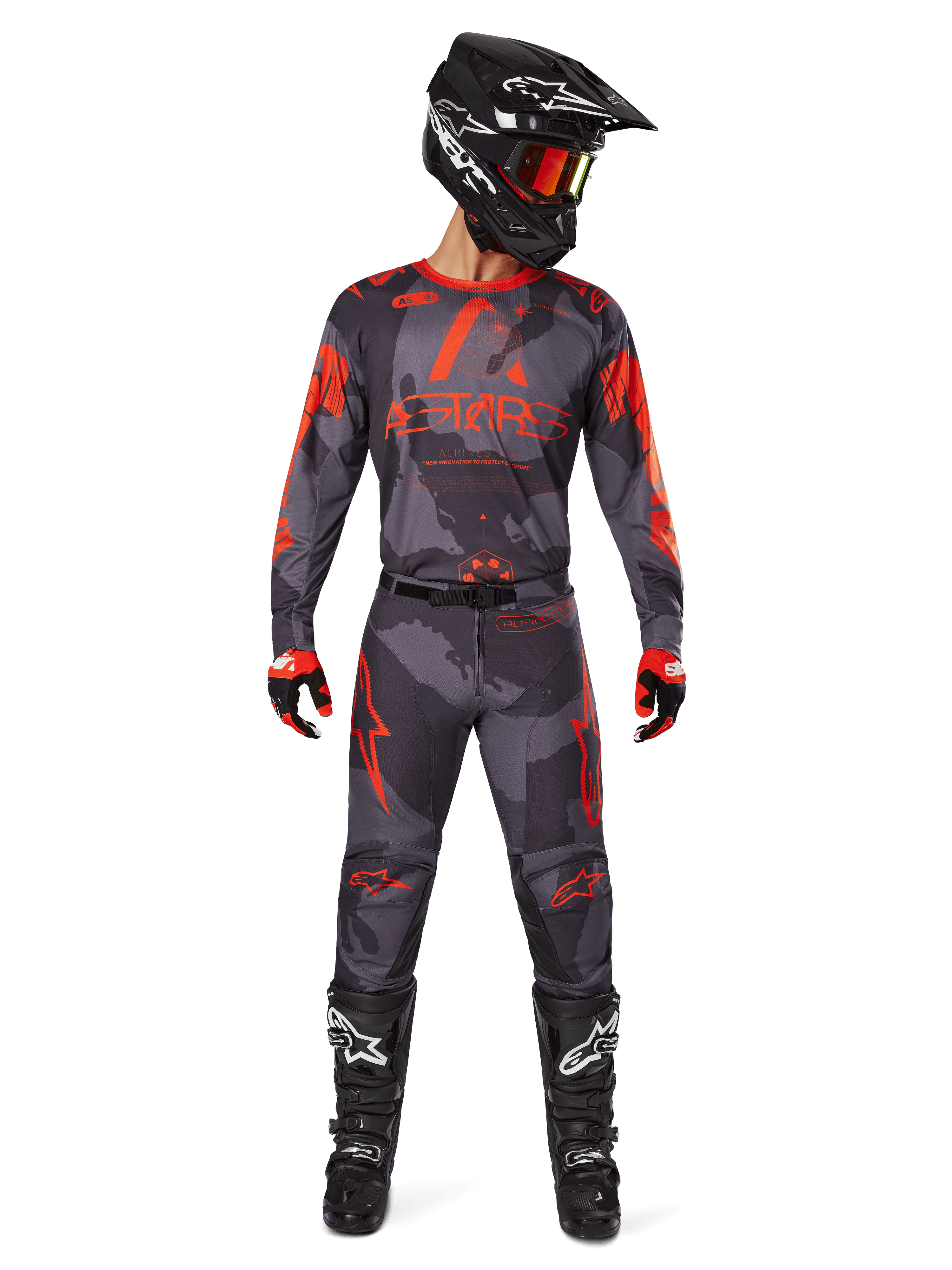 Motocyklista motocrossowy w koszulce Alpinestars 2025 Racer Hollow i dopasowanych spodniach w kolorze szarym camo z pomarańczowym fluo, kompletny zestaw z czarnym kaskiem, goglami, rękawicami i butami, wzór moro i wyraziste pomarańczowe logo.
