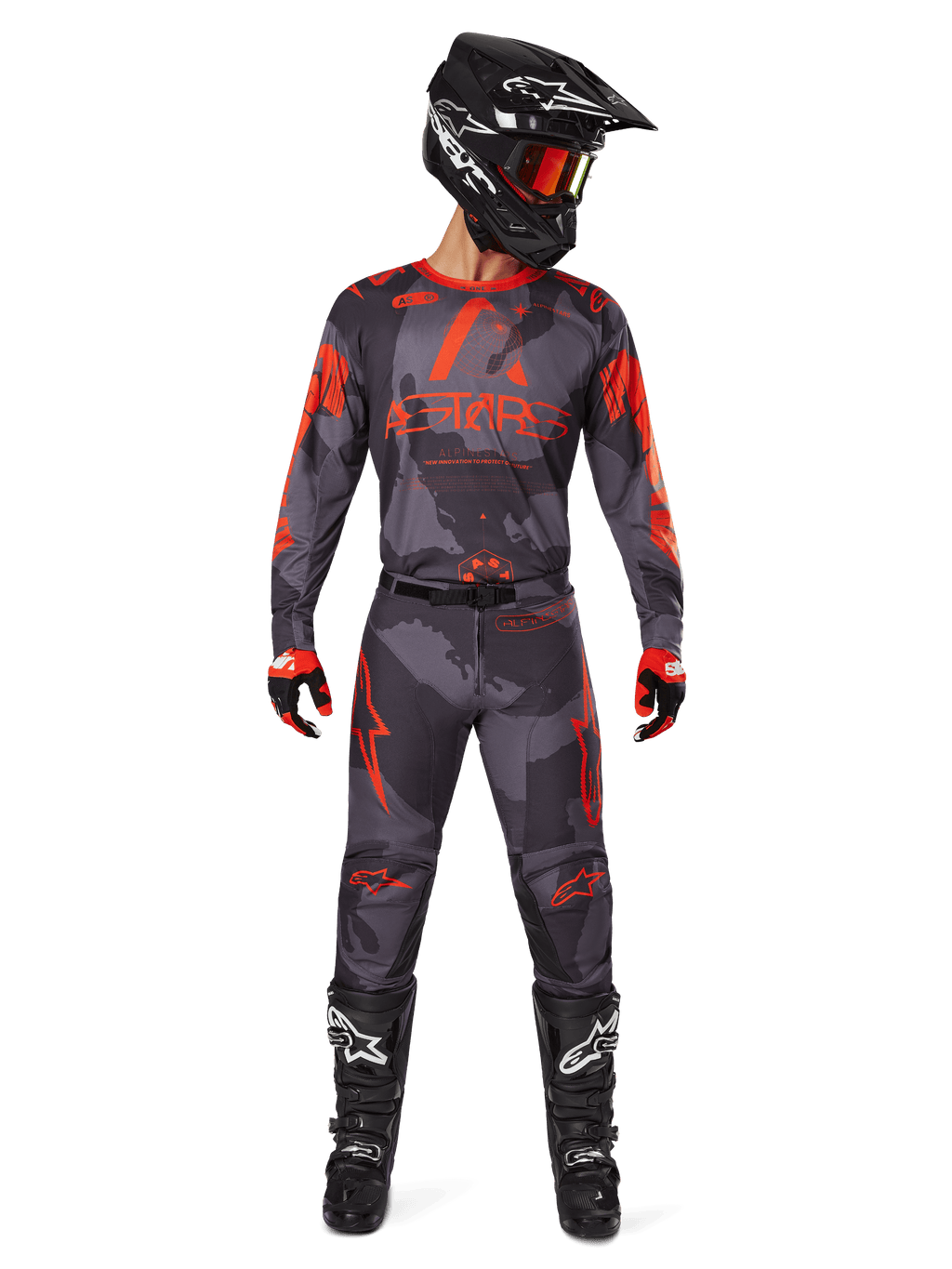 Zestaw Alpinestars 2025 Racer Hollow, zawodnik motocrossowy w koszulce i spodniach w szarym kamuflażu z jaskrawopomarańczowymi akcentami, czarny kask z pomarańczowymi goglami, czerwono-czarne rękawice, czarne buty z białym logo, pełny strój wyścigowy off-road