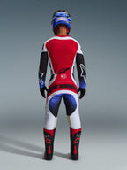 Alpinestars 2026 Techstar Knif Jersey, koszulka motocrossowa, czarno-biało-czerwona, widok z tyłu na zawodniku w dopasowanych spodniach i sprzęcie, jaskrawoczerwony panel tylny, białe spodnie z niebieskimi gradientami i czerwonym brandingiem, profesjonalny zestaw wyścigowy off-road