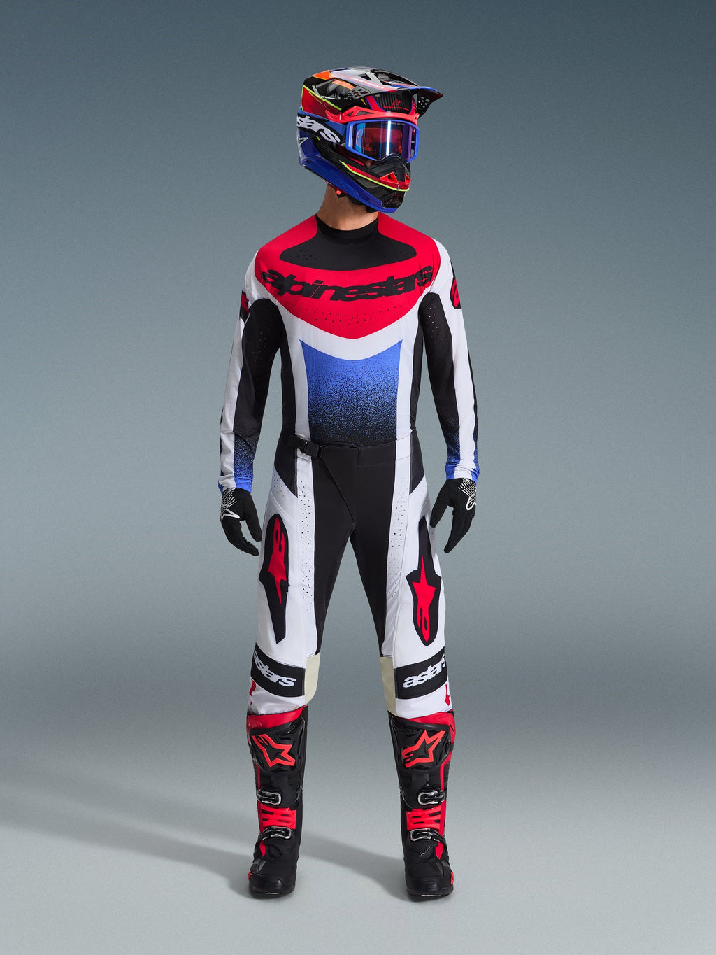 Koszulka Alpinestars 2026 Techstar Knif, koszulka motocrossowa w kolorach białym, czarnym, czerwonym i niebieskim z niebieską grafiką gradientową, część kompletnego zestawu off-road z pasującymi spodniami, czarno-czerwonymi butami i kaskiem z goglami.