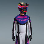 Zestaw Alpinestars Techstar Knif 2026, zawodnik motocrossowy w bluzie z niebiesko-różową grafiką i białym korpusem, białe spodnie z czarnymi panelami i różowym logo, fioletowo-różowy kask z dopasowanymi goglami, czarne rękawice, profesjonalny strój do wyścigów terenowych