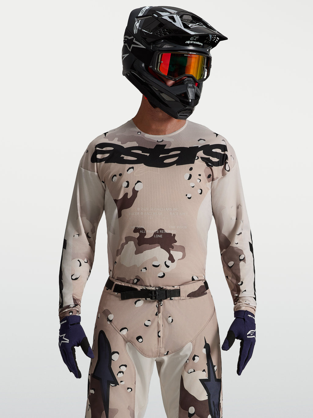 Alpinestars Koszulka Racer Lone, męska koszulka MX, pustynny kamuflaż i czarny, na modelu z kaskiem i goglami.