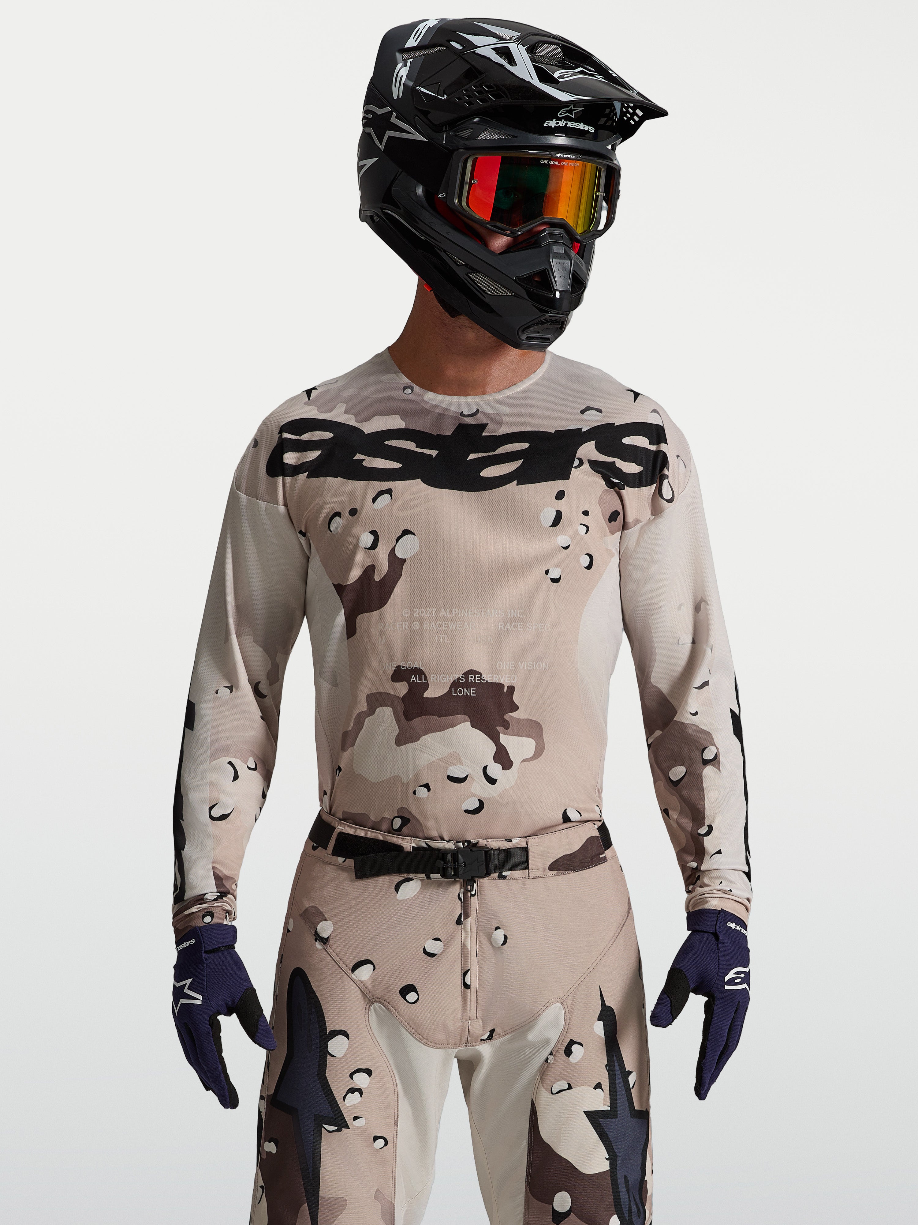 Alpinestars Koszulka Racer Lone, męska koszulka MX, pustynny kamuflaż i czarny, na modelu z kaskiem i goglami.