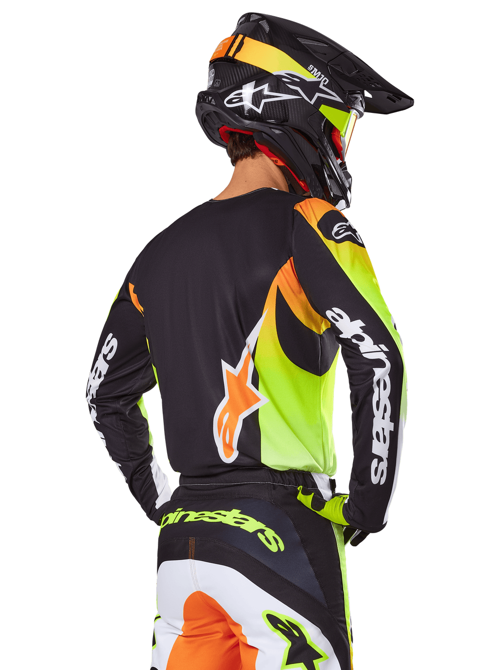 Motocyklista motocrossowy widziany od tyłu w zestawie Alpinestars 2025 Fluid Wurx, czarna koszulka z wyrazistymi neonowo-żółtymi i pomarańczowymi grafikami, dopasowane spodnie z białymi i pomarańczowymi panelami, czarny kask z neonowymi akcentami, wyraźny branding Alpinestars na rękawach i siedzeniu