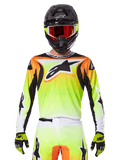 Koszulka Alpinestars Fluid Wurx 2025, koszulka motocrossowa, neonowożółta, pomarańczowa i biała, noszona z dopasowanymi spodniami i czarnym kaskiem z czerwonymi goglami, kompletny zestaw odzieży MX na motocykliście