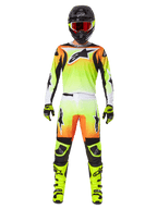 Zawodnik motocrossowy w pełnym stroju wyścigowym, zestaw Alpinestars 2025 Fluid Wurx, żółto-czarny z pomarańczowymi i białymi akcentami, koszulka z dużym logo z przodu, pasujące spodnie, czarny kask z goglami z czerwonymi szybkami, neonowożółte buty, profesjonalny komplet odzieży do wyścigów terenowych