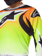Koszulka Alpinestars Fluid Wurx 2025, koszulka motocrossowa, neonowożółta z czarną i pomarańczową grafiką, duże czarne logo Alpinestars na klatce piersiowej i ramieniu, noszona przez motocyklistę w czarnym kasku
