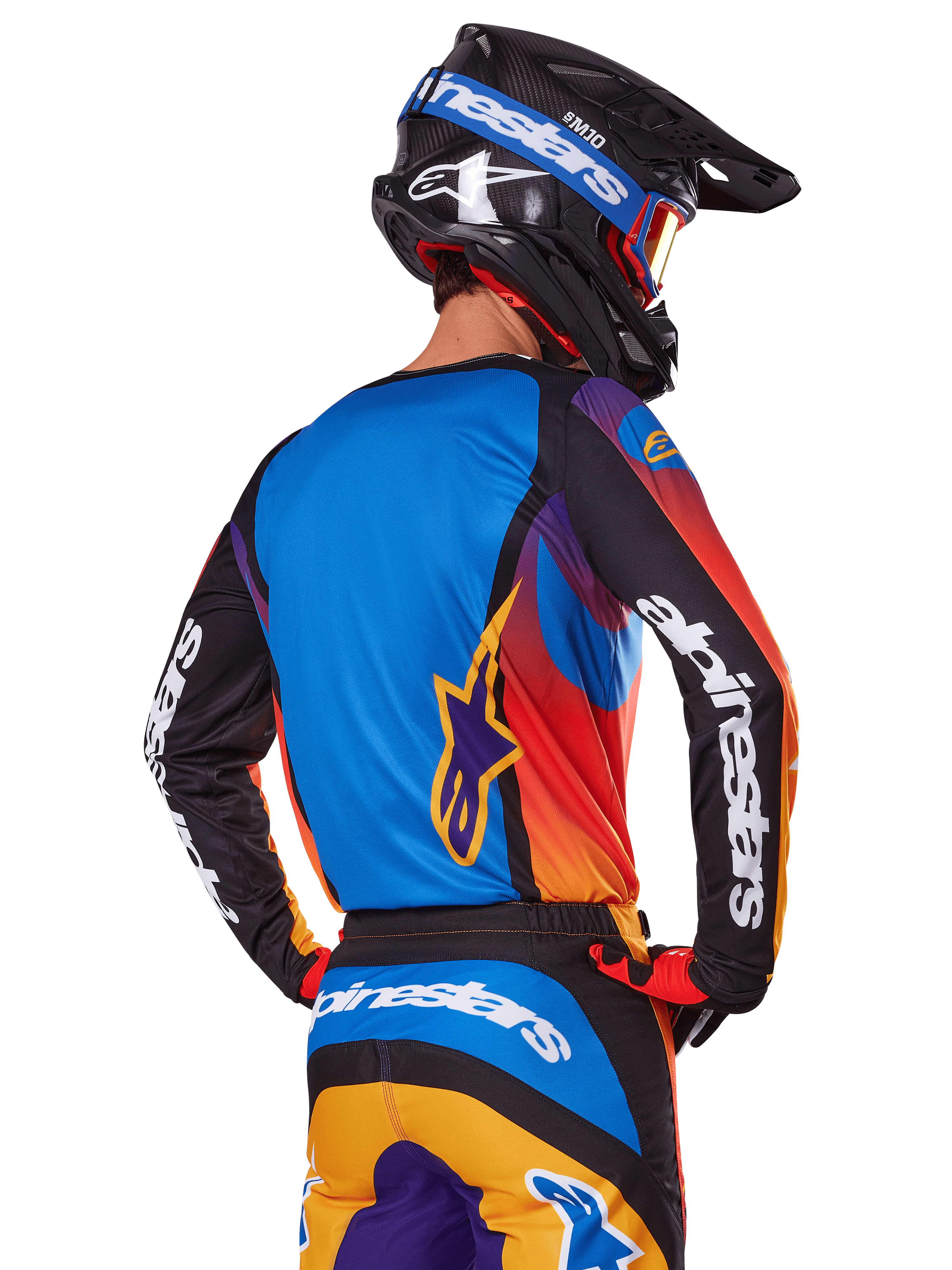 Motocrossowiec widziany od tyłu w zestawie Alpinestars 2025 Fluid Wurx, wielokolorowa koszulka z niebieskim tyłem i czarnymi rękawami z białym logo, pasujące pomarańczowo-niebieskie spodnie, czarno-niebieski kask z pomarańczowymi goglami, spójny strój do wyścigów terenowych.