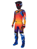 Zestaw Alpinestars 2025 Fluid Wurx, koszulka i spodnie motocrossowe z pomarańczowo-czerwono-fioletowym gradientem i niebiesko-żółtymi wzorami gwiazd, czarny kask, czerwone gogle, czerwono-czarne rękawice i niebieskie buty, odzież wyścigowa o wysokiej widoczności