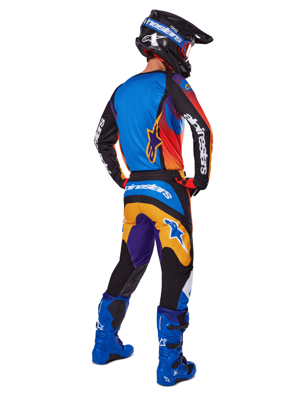 Motocyklista motocrossowy widziany od tyłu w zestawie Alpinestars 2025 Fluid Wurx, wielokolorowa koszulka z niebieskimi, pomarańczowymi i fioletowymi panelami, pasujące spodnie z białym logo Alpinestars na siedzeniu, jaskrawoniebieskie buty i czarny kask, skoordynowany strój do wyścigów terenowych