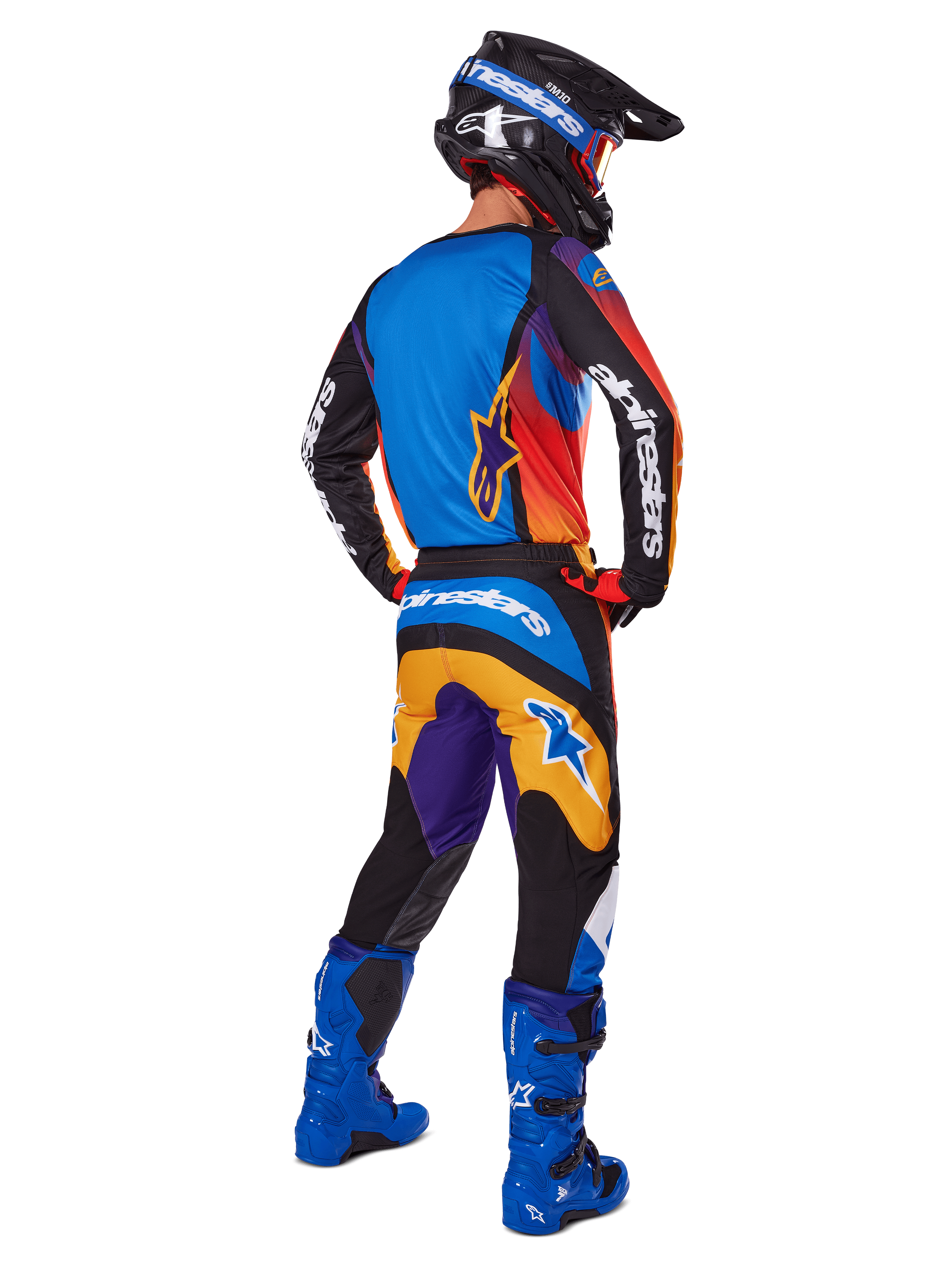 Motocyklista motocrossowy widziany od tyłu w zestawie Alpinestars 2025 Fluid Wurx, wielokolorowa koszulka z niebieskimi, pomarańczowymi i fioletowymi panelami, pasujące spodnie z białym logo Alpinestars na siedzeniu, jaskrawoniebieskie buty i czarny kask, skoordynowany strój do wyścigów terenowych