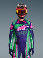 Zestaw Alpinestars Techstar Nomur 2026, zawodnik motocrossowy w jaskrawozielonej i fioletowej koszulce wyścigowej z różowymi akcentami, pasujący komplet z wielokolorowym kaskiem i goglami, wyczynowy strój do jazdy terenowej
