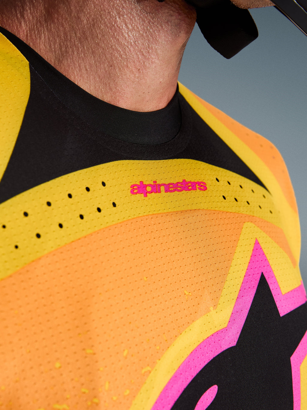 Alpinestars 2026 Techstar Nomur Jersey, koszulka motocrossowa, pomarańczowo-żółto-różowa, zbliżenie na detale klatki piersiowej i kołnierzyka, laserowo wycinana wentylacja, różowe logo i oddychająca tkanina siateczkowa
