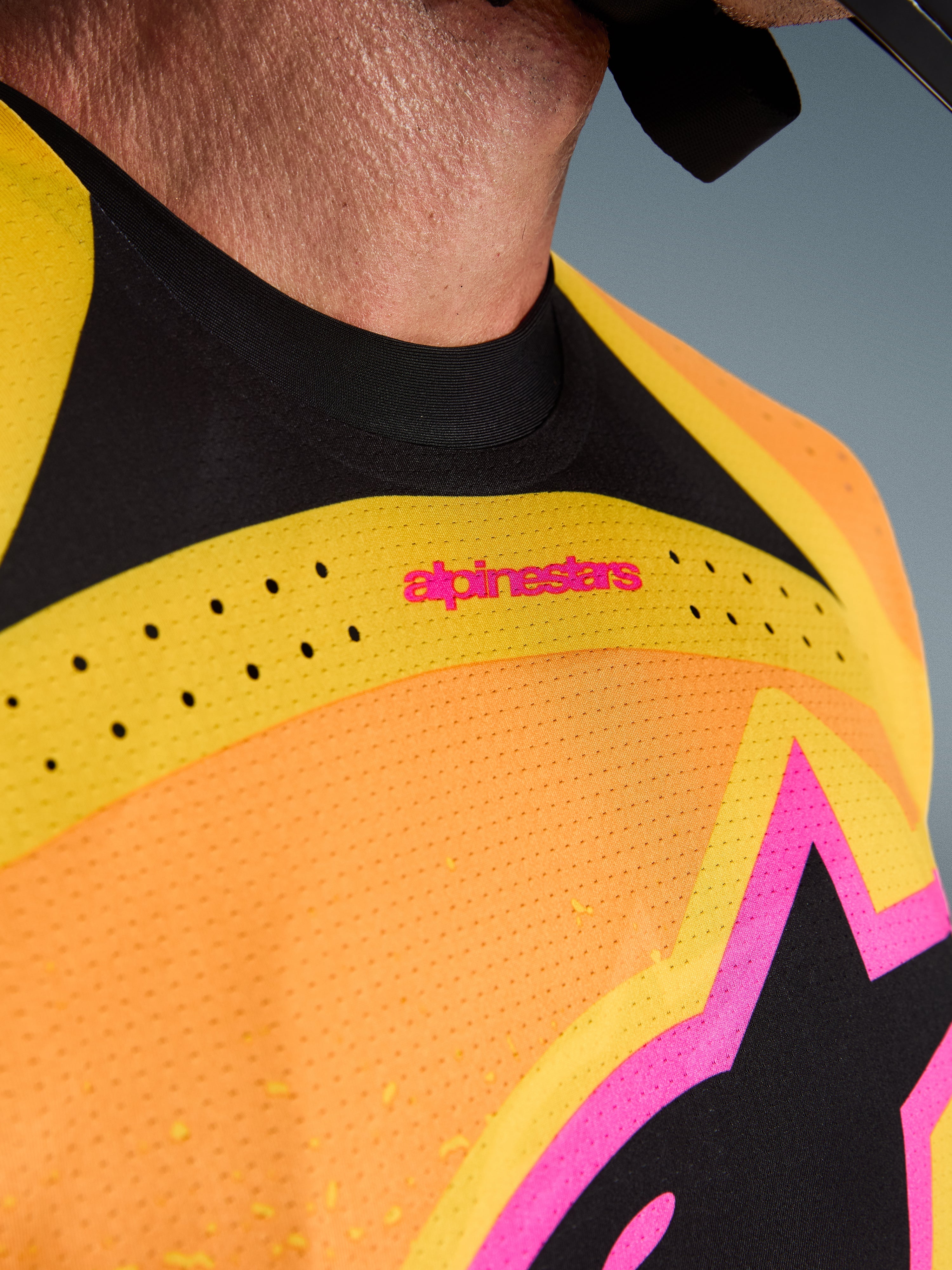 Alpinestars 2026 Techstar Nomur Jersey, koszulka motocrossowa, pomarańczowo-żółto-różowa, zbliżenie na detale klatki piersiowej i kołnierzyka, laserowo wycinana wentylacja, różowe logo i oddychająca tkanina siateczkowa