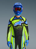 Zawodnik motocrossowy w koszulce Alpinestars 2026 Techstar Nomur w kolorze ciemnogranatowym i neonowym żółtym z niebieskimi akcentami, z dużym niebieskim logo na klatce piersiowej, dopasowanym niebieskim kaskiem i goglami, profesjonalny strój wyścigowy do rywalizacji off-road