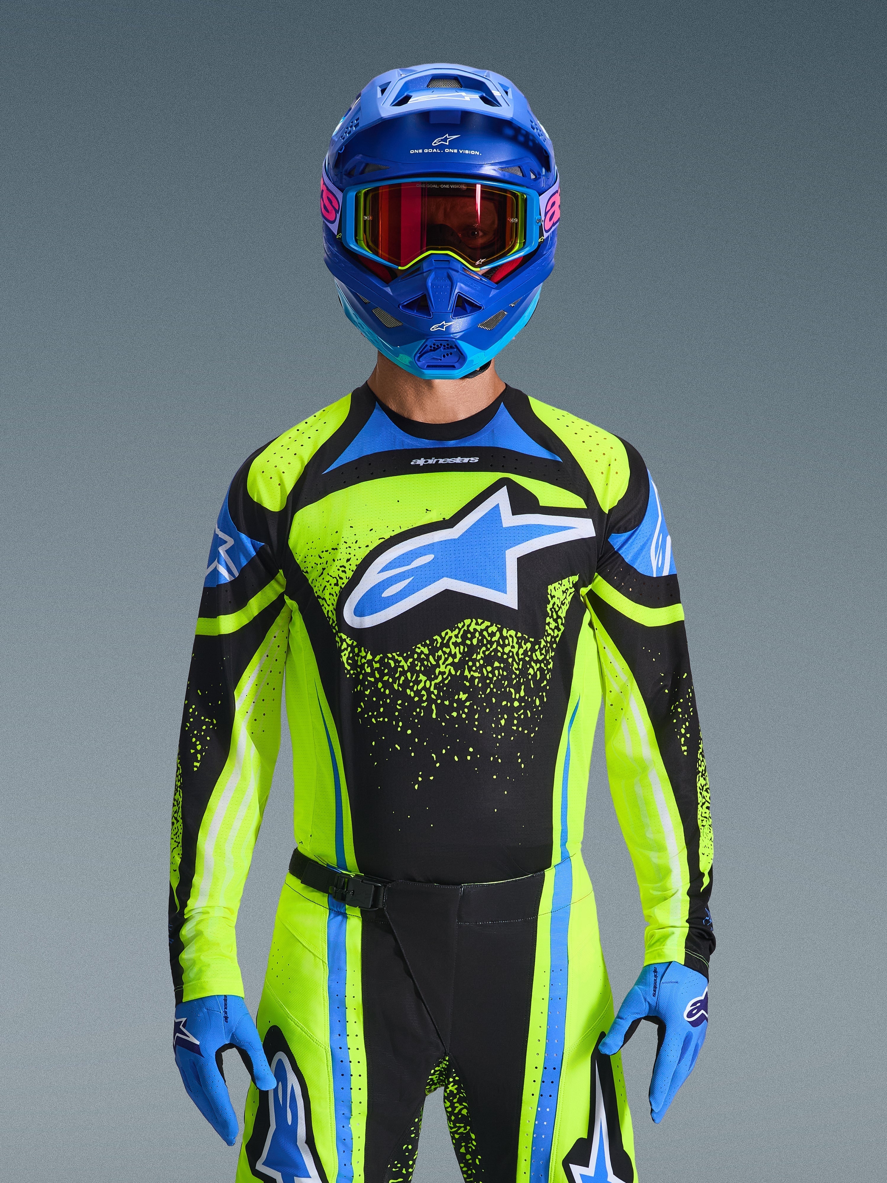 Zawodnik motocrossowy w koszulce Alpinestars 2026 Techstar Nomur w kolorze ciemnogranatowym i neonowym żółtym z niebieskimi akcentami, z dużym niebieskim logo na klatce piersiowej, dopasowanym niebieskim kaskiem i goglami, profesjonalny strój wyścigowy do rywalizacji off-road