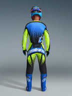 Zestaw Alpinestars 2026 Techstar Nomur, widok z tyłu zawodnika motocrossowego, niebiesko-neonowożółta koszulka z czarnymi akcentami o wzorze sprayu, pasujące neonowożółto-czarne spodnie z dużym niebieskim logo „astars” na siedzeniu, niebieskie buty z białym logo, niebiesko-czarny kask, pełny profesjonalny strój wyścigowy zaprojektowany dla wydajności i widoczności