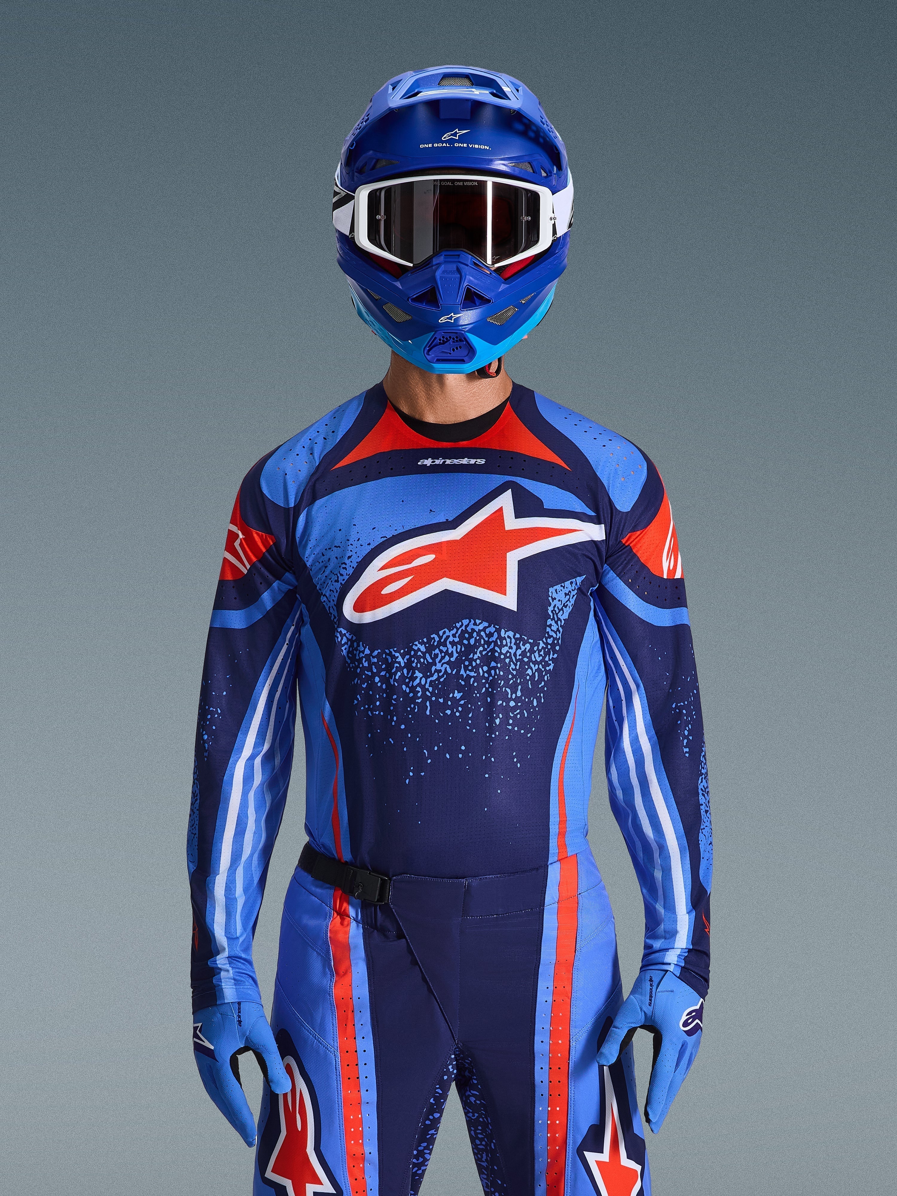 Alpinestars 2026 Techstar Nomur Jersey, koszulka motocrossowa, ciemnogranatowa, pomarańczowa i niebieska UCLA, noszona z pasującymi spodniami, niebieskim kaskiem i rękawicami, z białym logo gwiazdy na piersi, dynamicznymi liniami i kropkowanymi wzorami