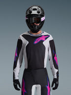 Zestaw Alpinestars 2026 Fluid Grid, zawodnik motocrossowy w czarno-biało-różowej koszulce i pasujących spodniach, czarny kask z różowymi i białymi akcentami, profesjonalny strój wyścigowy do jazdy w terenie