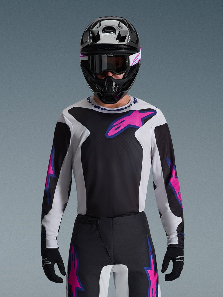 Alpinestars 2026 Fluid Grid Jersey, koszulka motocrossowa, czarna, jasnoszara i fioletowa, noszona przez motocyklistę z dopasowanymi spodniami off-road, czarnym kaskiem i goglami, kompletny wyczynowy zestaw odzieży wyścigowej