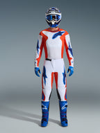 Alpinestars 2026 Fluid Grid Gear Set, motocyklista motocrossowy w pełnym rynsztunku, biała koszulka i spodnie z pomarańczowymi i błękitnymi akcentami, pasujący niebiesko-biały kask z niebieskimi goglami, niebieskie rękawice i niebieskie buty motocrossowe, dopasowany strój do wyścigów terenowych