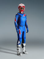 Motocrossowiec w koszulce Alpinestars 2026 Fluid Grid w kolorze niebiesko-czerwonym, dopasowane spodnie motocrossowe, biało-czarne buty i czerwono-biały kask, profesjonalny zestaw odzieży do jazdy off-road