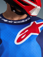 Alpinestars 2026 Fluid Grid Jersey, niebiesko-czerwona, zbliżenie na klatkę piersiową i sportowy kołnierzyk, duże czerwono-białe logo gwiazdy Alpinestars, branding Alpinestars na dekolcie, noszona z czerwono-białym kaskiem
