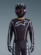 Zestaw Alpinestars 2026 Fluid Apex, koszulka i spodnie motocrossowe w kolorze czarno-białym, duże logo na klatce piersiowej i geometryczne wzory linii, czarny kask i różowe gogle, profesjonalna odzież do wyścigów motocrossowych.